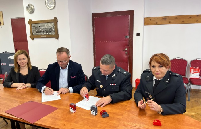 Wójt oraz strażak podpisują dokumenty przy stole