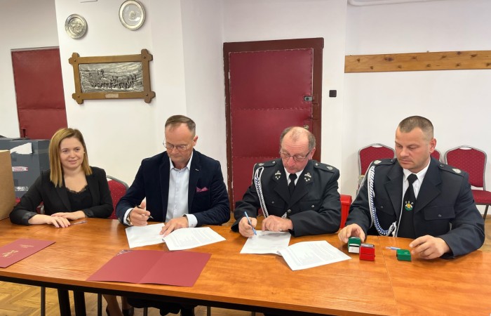 Wójt oraz strażak podpisują dokumenty przy stole